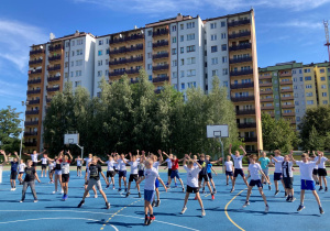 Uczniowie ćwiczący na boisku szkolny w strojach sportowych