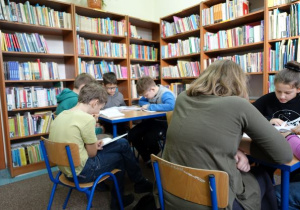 Dzieci siedzą w bibliotece i czytają książki