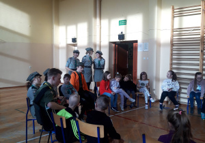 Dzieci z harcerzami siedzą na krzesłach w kręgu