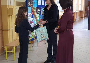 Dwie panie wręczają uczennicy nagrodę