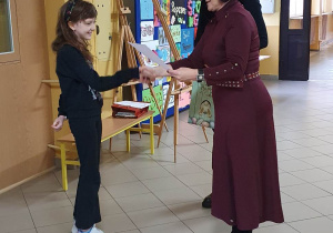 Dwie panie wręczają uczennicy nagrodę