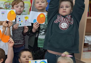 Dzieci trzymają wysoko nad głowami kolorowe kartki z pisankami