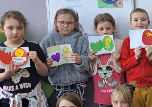 Dzieci trzymają wysoko nad głowami kolorowe kartki z pisankami