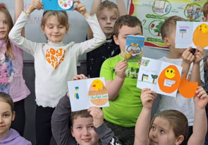 Dzieci trzymają wysoko nad głowami kolorowe kartki z pisankami