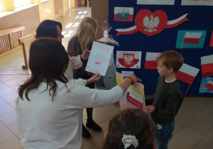 Panie oglądają prace z biało-czerwonymi flagami, dzieci stoją obok.