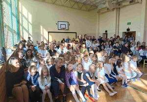 Dzieci i dorośli siedzący na ławeczkach.