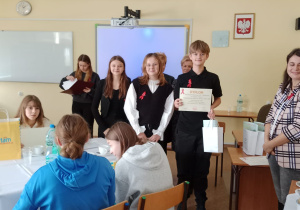 Dzieci stoją przy stoliku, chłopiec trzyma dyplom