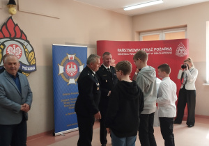 Chłopcy stoją przodem do mężczyzn w mundurach strażaka