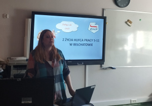Pani przy komputerze stoi na tle ekranu