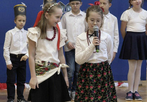 Uśmiechnięte dziewczynki w stroju galowym mówią do mikrofonu