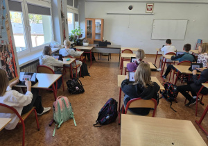 Uczniowie siedzą w ławkach i używają tabletów do nauki