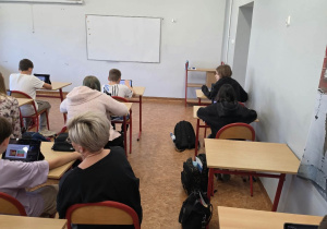 Uczniowie siedzą w ławkach i używają tabletów do nauki