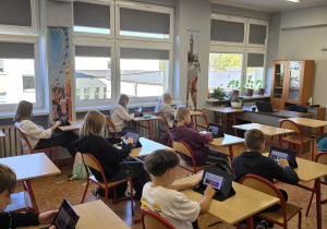 Uczniowie siedzą w ławkach i używają tabletów do nauki