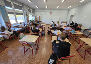 Uczniowie siedzą w ławkach i używają tabletów do nauki