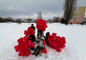 dzieci siedzące na śniegu, czerwone balony w kształcie serc