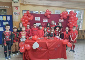 Dzieci w czerwonych strojach na tle balonów
