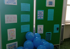 Wystawa na zielonym płótnie z leżącymi na podłodze Niebieskimi balonami z napisem 2 kwietnia Światowy Dzień Świadomości Autyzmu