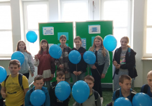 Dziecie na tle wystawy z trzymającymi w rękach niebieskie balony z napisem 2 kwietnia Światowy Dzień Świadomości Autyzmu.