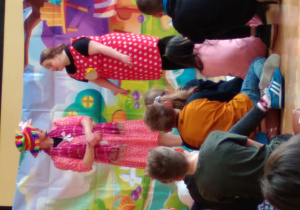 Dzieci siedzące na podłodze, a przed nimi dwa kolorowe stworki
