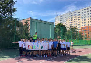 Uczniowie w strojach sportowych trzymające bilbord z napisem Fair Play