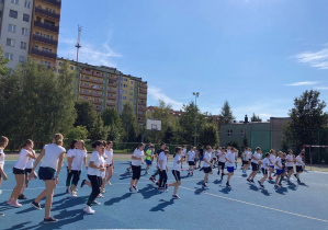 Uczniowie w strojach sportowych wykonujący ćwiczenia na boisku szkolnym