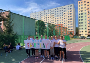 Uczniowie w strojach sportowych trzymające bilbord z napisem Fair Play