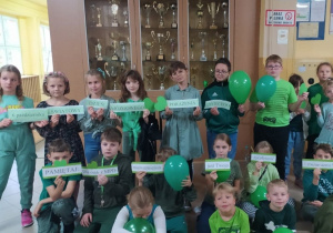 Dzieci ubrane w zielone stroje trzymające balony i napis 6 października  Światowy Dzień Mózgowego Porażenia Dziecięcego.