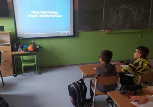 Tablica interaktywna z wyświetlanym filmem, obok uczniowie w ławkach