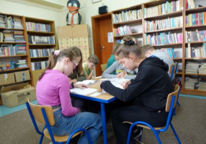 Dzieci siedzą w bibliotece i czytają książki