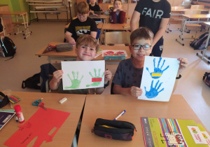 Chłopcy trzymające prace z odciśniętymi dłońmi w kolorze niebieskim