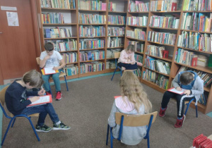 Dzieci siedzą na krzesłach w bibliotece