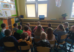 Dzieci siedzą na krzesłach i oglądają pokaz na ekranie laptopa