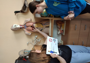 Dziewczynki stoją przy manekinie i wskazują jego organach wewnętrznych płuca