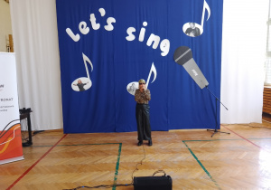 Dziewczyna z mikrofonem na tle napisu Let's Sing