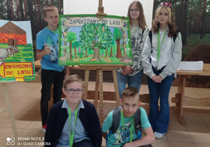 Młodzież stoi przy sztaludze z rysunkiem o lesie