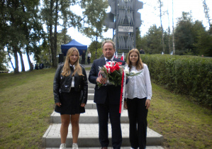 2 dziewczyny z mężczyzną z kwiatami na tle pomnika