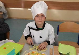 Chłopiec w czapce kucharza przygotowuje jedzenie.