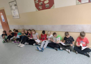 Dzieci siedzące na podłodze pod ścianą czytają książki
