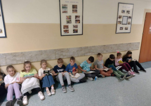 Dzieci siedzące na podłodze pod ścianą czytają książki