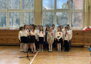 Dzieci z przypiętymi kotylionami śpiewają piosenkę