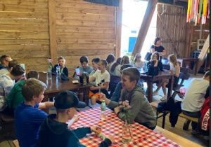 Dzieci siedzą przy stołach w stodole