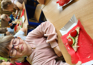 Dziewczynka w okularach z kanapką w kształcie trójkąta z pomidorkami