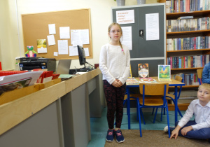 Chłopiec stoi w bibliotece przy biurku