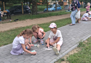 Dzieci na dworze malują na chodniku kredą