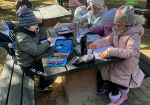 Uśmiechnięte dzieci siedzą przy stoliku w lesie i kolorują obrazek