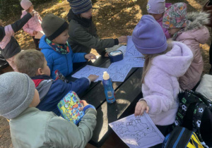 Uśmiechnięte dzieci siedzą przy stoliku w lesie i kolorują obrazek