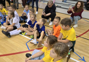 Radosne dzieci w strojach sportowych siedzą na podłodze