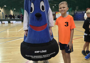 Chłopiec w stroju sportowym stoi obok maskotki policjanta