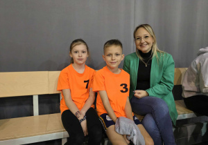 Radosne dzieci w strojach sportowych siedzą z kobietą na ławce