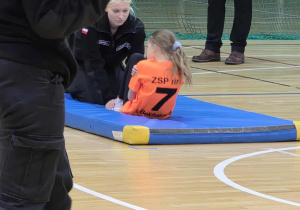 dziewczynka w stroju sportowy ćwiczy na materacu z kobietą w stroju policjanta